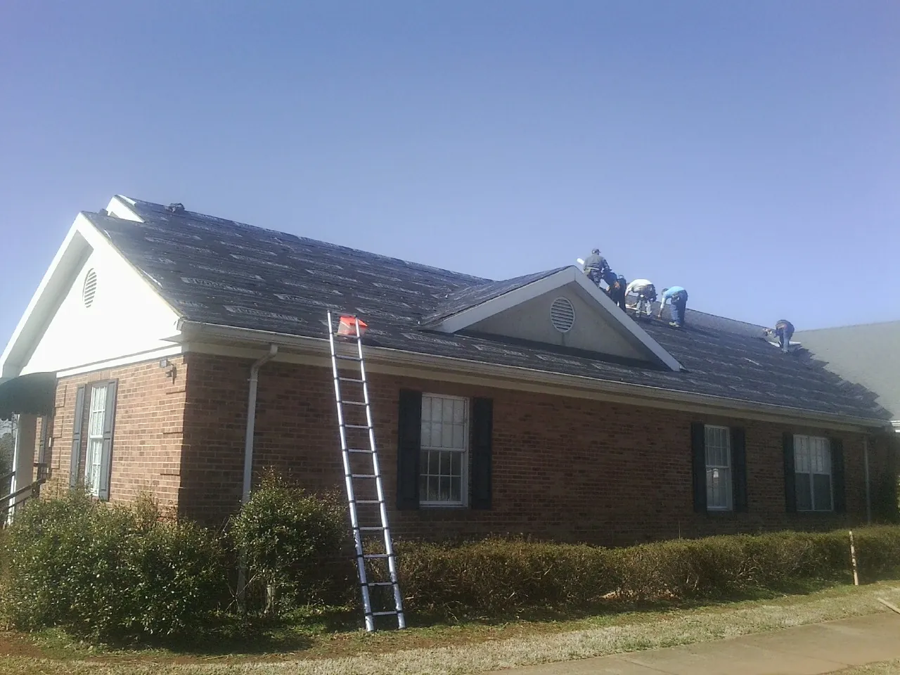 Crew tearing shingles off a brick ranch roof with a ladder set — Emergency Roof Repair work by our crew in Mentone