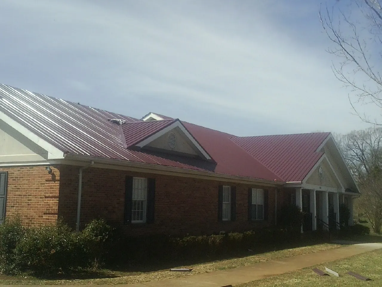 Red metal roof with gabled entries on a long brick building, from a Hail Damage Roof Repair job in Mentone